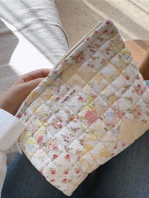 Hand holding a large quilted yellow floral makeup bag with patchwork design and “simple wish” label