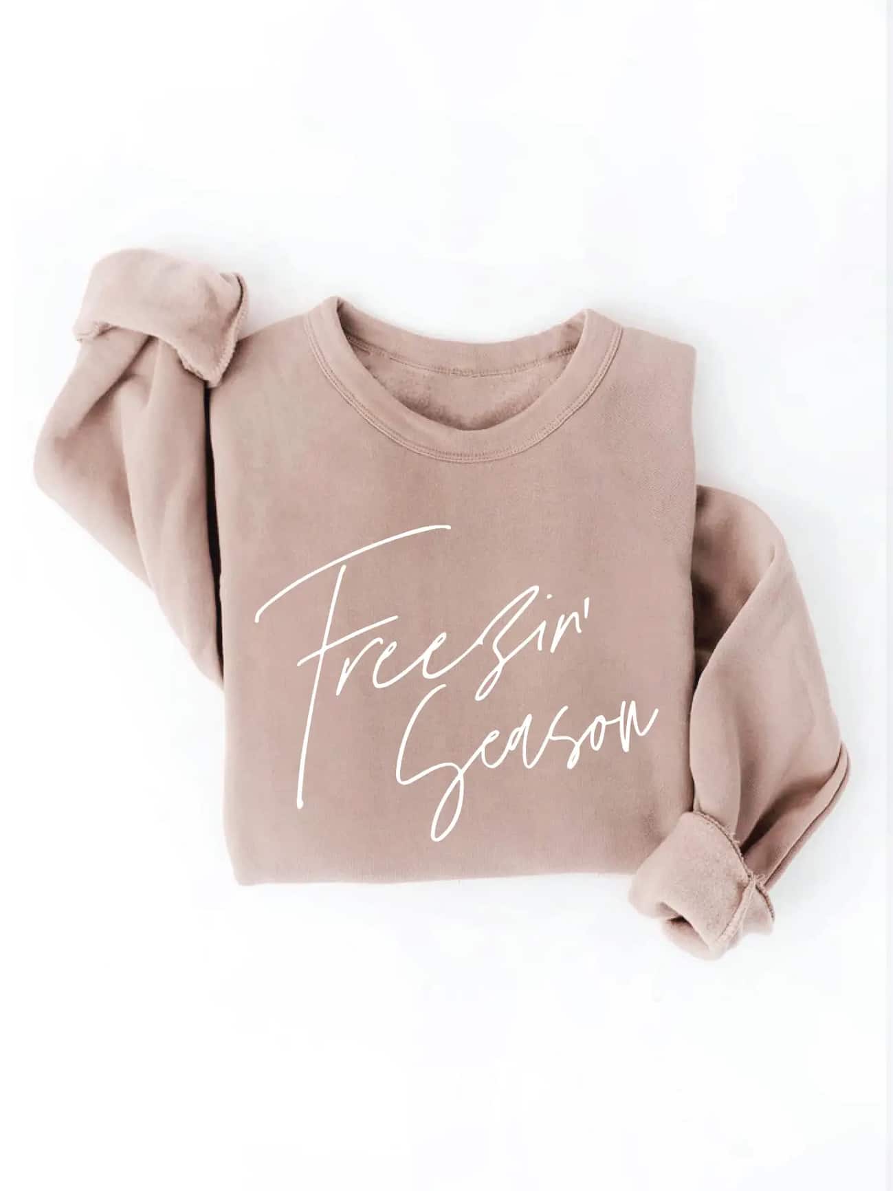 Tan crewneck sweatshirt with white script text reading “Freezin’ Season,” styled with ribbed cuffs and a cozy relaxed fit.
