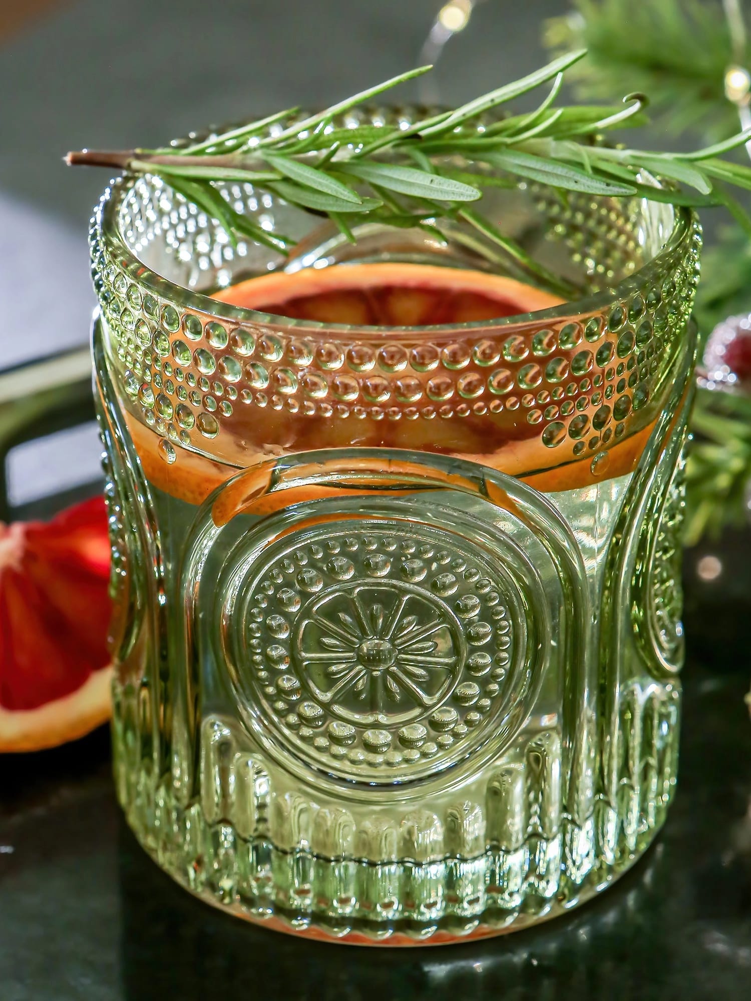 Green retro arched drinking glass featuring a fresh cocktail with grapefruit slice and rosemary garnish.