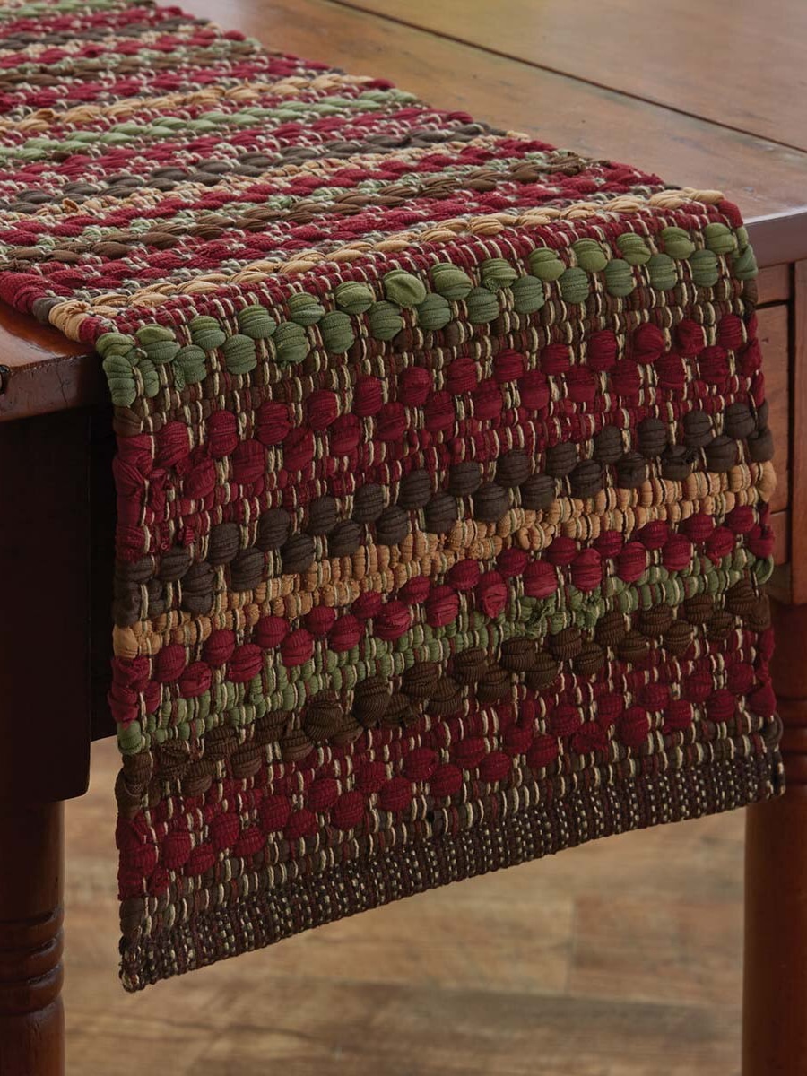 Handwoven cotton table runner in red, green, and brown tones styled with breakfast setting near Christmas tree.