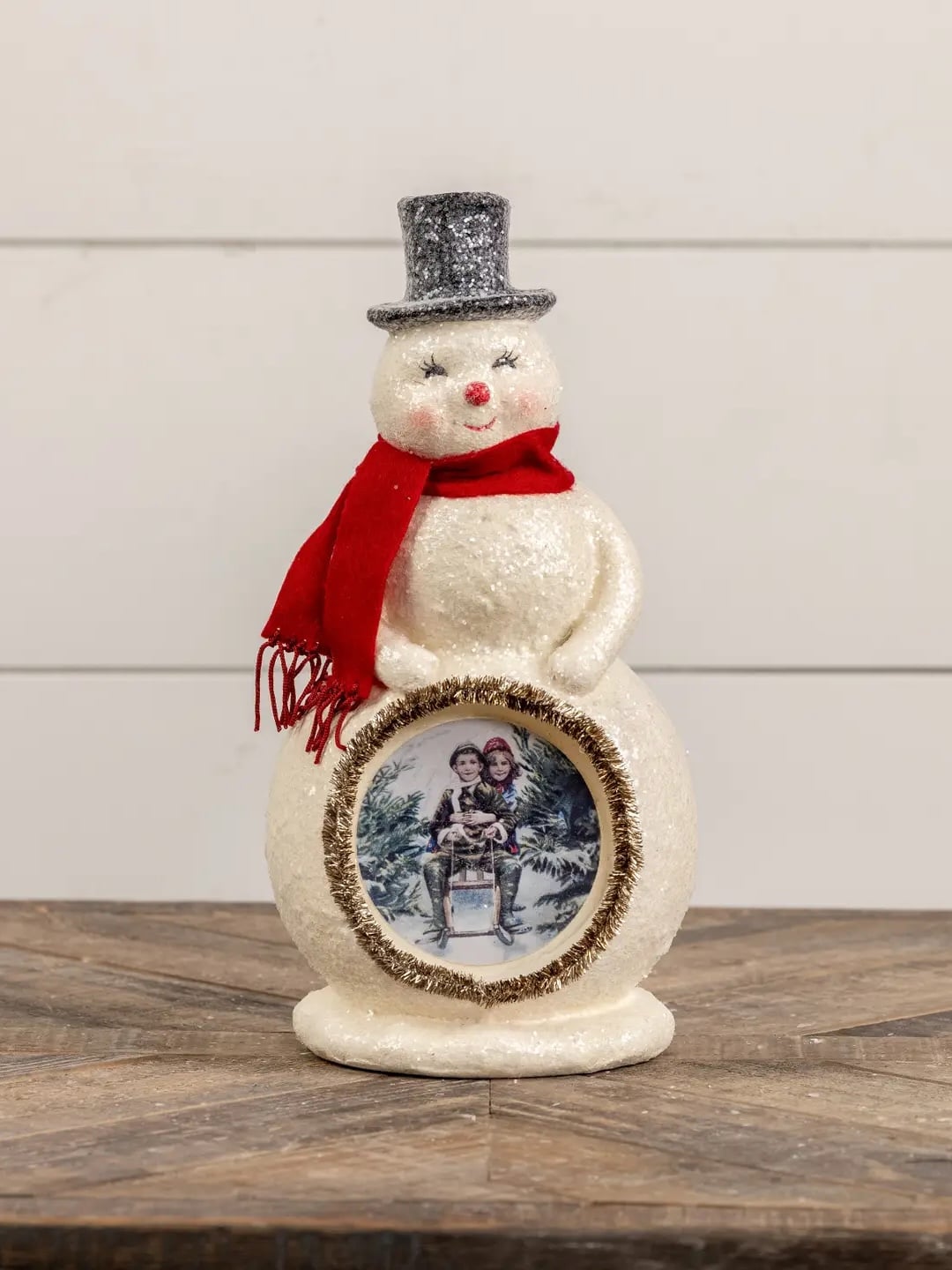 Handcrafted paper mache snowman wearing a red scarf and silver top hat, decorated with a classic vintage winter scene in the center.