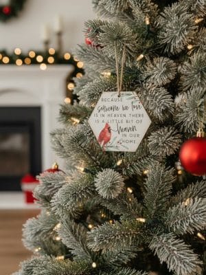 Cardinal “Someone We Love Is in Heaven” wooden ornament hanging on a lit Christmas tree with frosted branches.