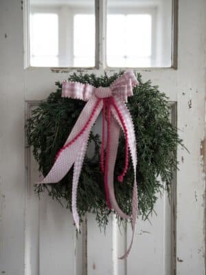 Draping Cedar Wreath with lush soft-touch cedar greenery on a rustic white door, shown with a pink gingham ribbon bow (bow not included).