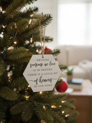 “Someone We Love is in Heaven” wooden hexagon ornament hanging on a Christmas tree with soft seasonal lights.