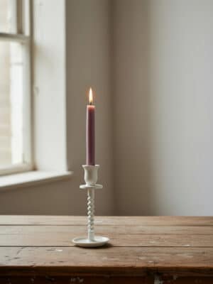 Off-white corkscrew taper candle holder small with lit mauve taper candle on a wooden table.