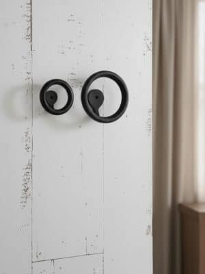 Small and large matte black round metal wall hooks mounted side by side on a white wall.
