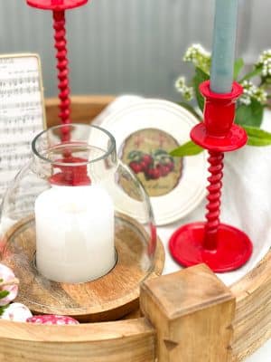 Small wood and glass hurricane candle holder styled with a lit white pillar candle next to a red corkscrew taper holder with a blue candle.