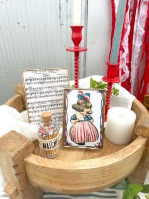 Industrial-style gold metal photo frames, red taper holders, and vintage matches styled in a wood pedestal with patriotic flair.