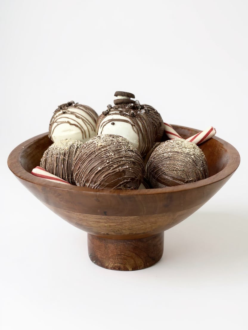 Large hand-carved mango wood footed bowl filled with chocolate-dipped treats and peppermint sticks on a white background.