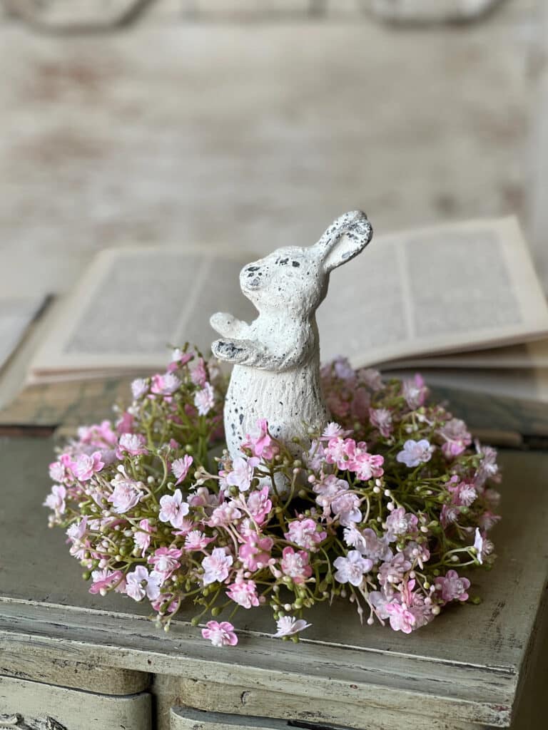 White Distressed Bunny Figurine nestled inside a pink floral candle ring on stacked vintage books for spring styling.