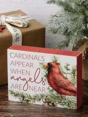 Cardinal box sign with evergreen accents displayed beside holiday décor and gifts.