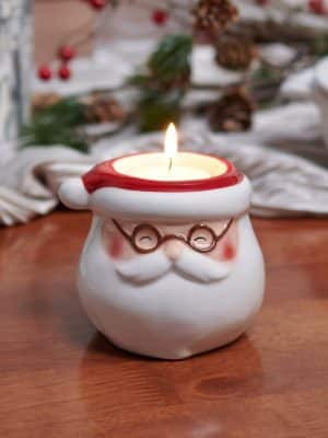 Santa tealight candle holder glowing with lit candle on holiday table.