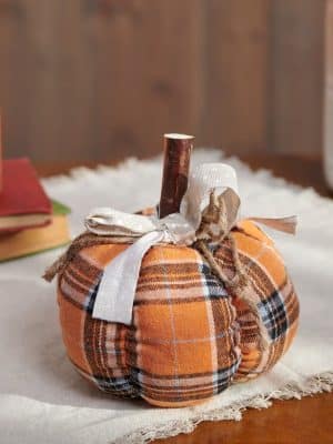 Cozy fall décor pumpkin in orange plaid fabric styled on a table.