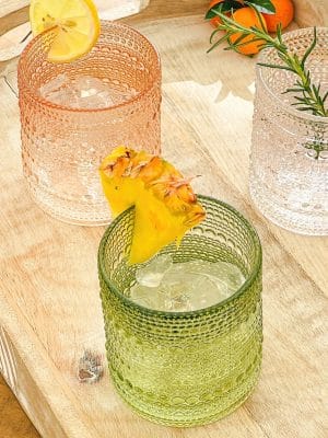 Rose gold and sage green beaded old fashion drinking glasses with ice and citrus garnishes.