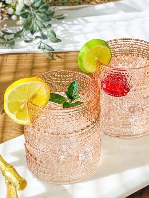 Rose gold beaded old fashion glasses with cocktails garnished with lemon, lime, and mint.