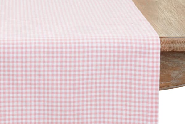Pink gingham table runner draped over the end of a wooden table, showing the soft cotton texture.