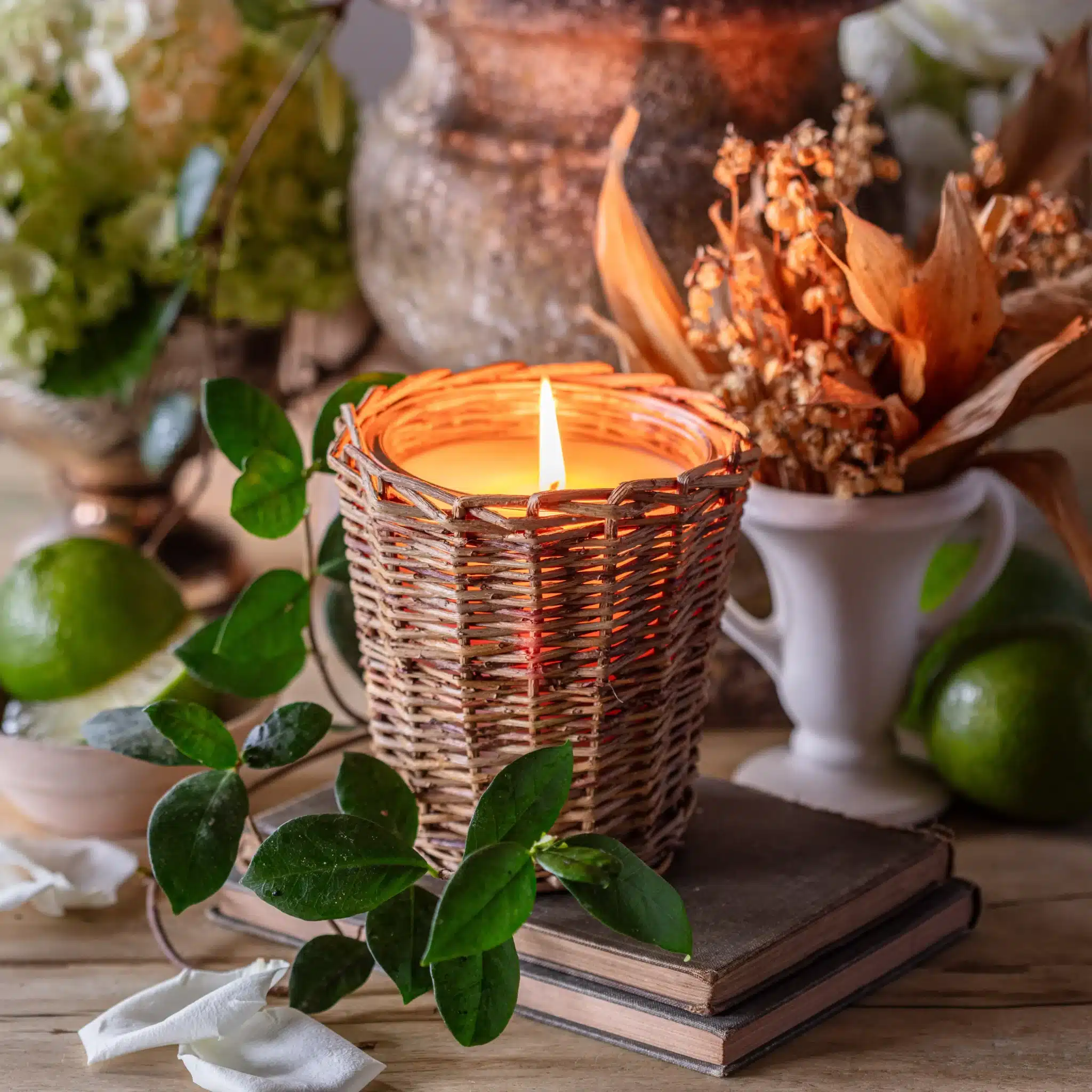 Wicker Chapel Candle in a natural woven holder with a lit flame, styled on stacked books with greenery for cozy farmhouse decor.