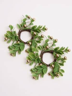 Set of two taper candle rings with green faux leaves and metallic gold berries arranged on natural brown stems.
