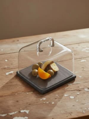 Angled view of the Marble Square Cloche Black with a hand-formed glass dome on a black marble base, styled with fruit.