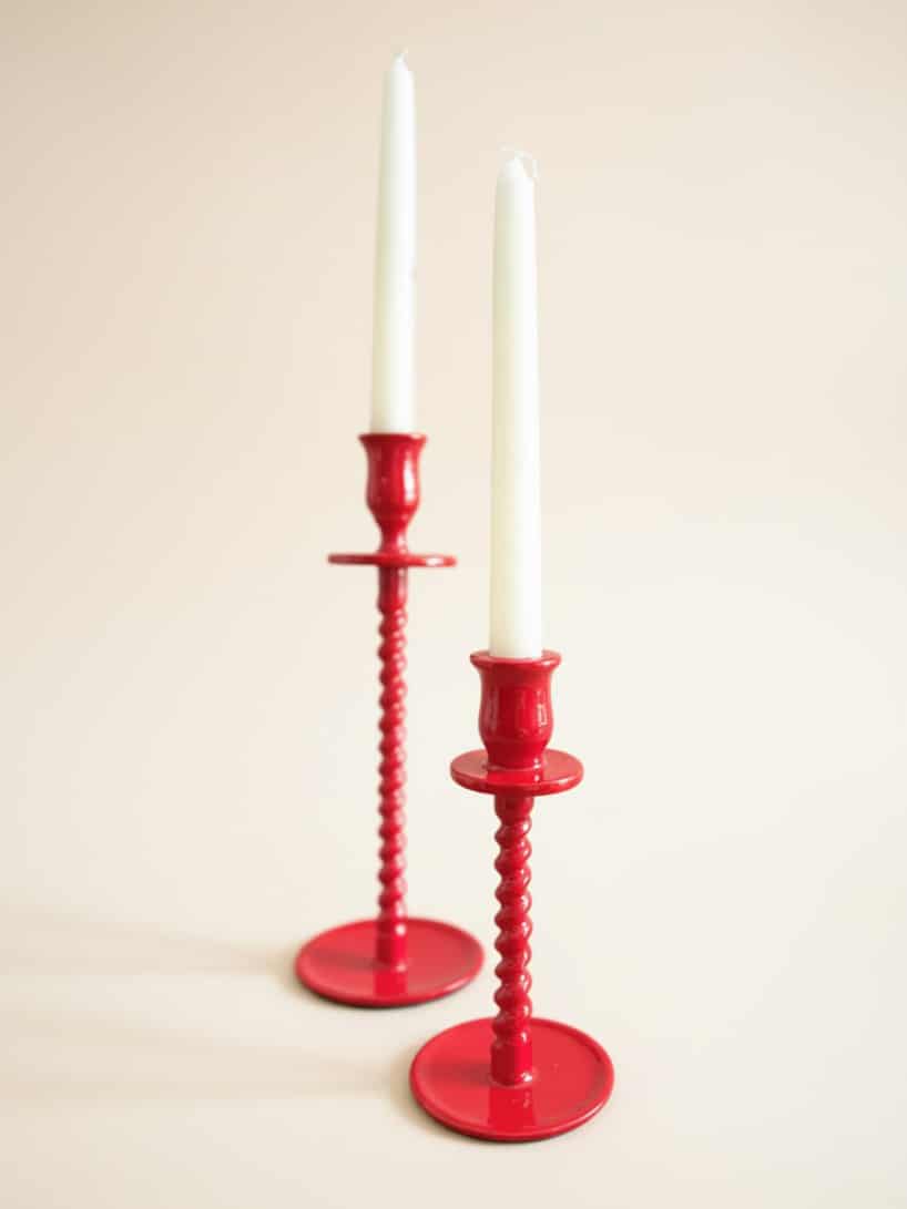 Small and large red corkscrew-style taper candle holders displayed together with ivory tapers on a clean neutral background.