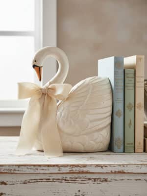 A white stoneware swan bookend with sculpted feathers styled beside a small stack of books on a rustic table.