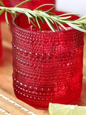 Red beaded old fashion drinking glass with rosemary garnish.
