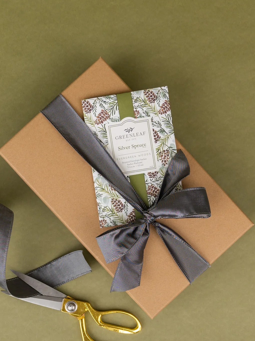 Gift-wrapped Silver Spruce scented sachet tied with ribbon on holiday box.