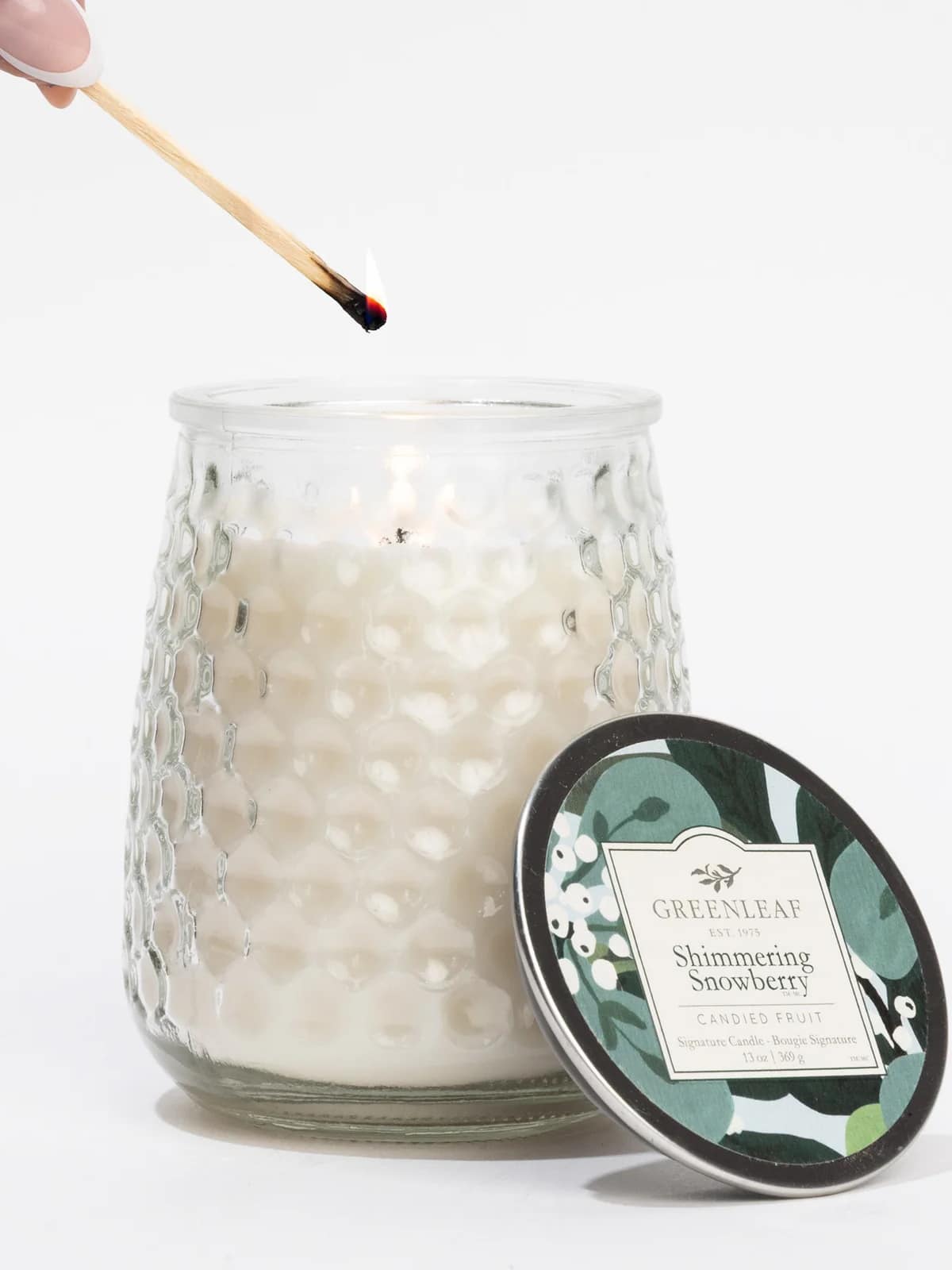 Shimmering Snowberry Signature Candle in hobnail glass jar being lit with a match.