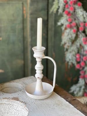 Vintage white chamberstick taper candle holder styled on a wooden surface with greenery and a soft distressed finish.