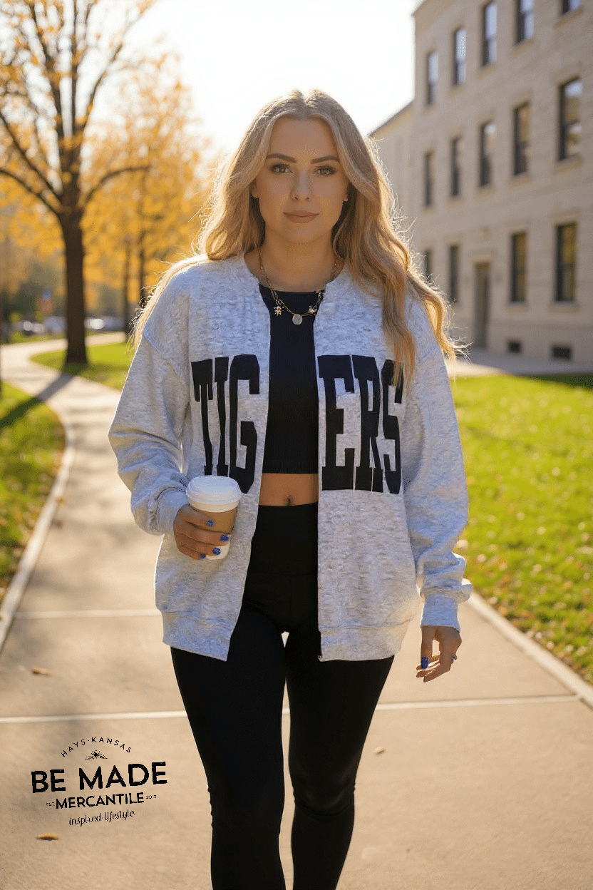 Woman walking outdoors in an ash gray oversized Tigers cardigan, holding a coffee cup.