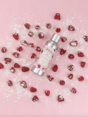Brambleberry Room Spray lying on a pink background surrounded by sugared raspberries.