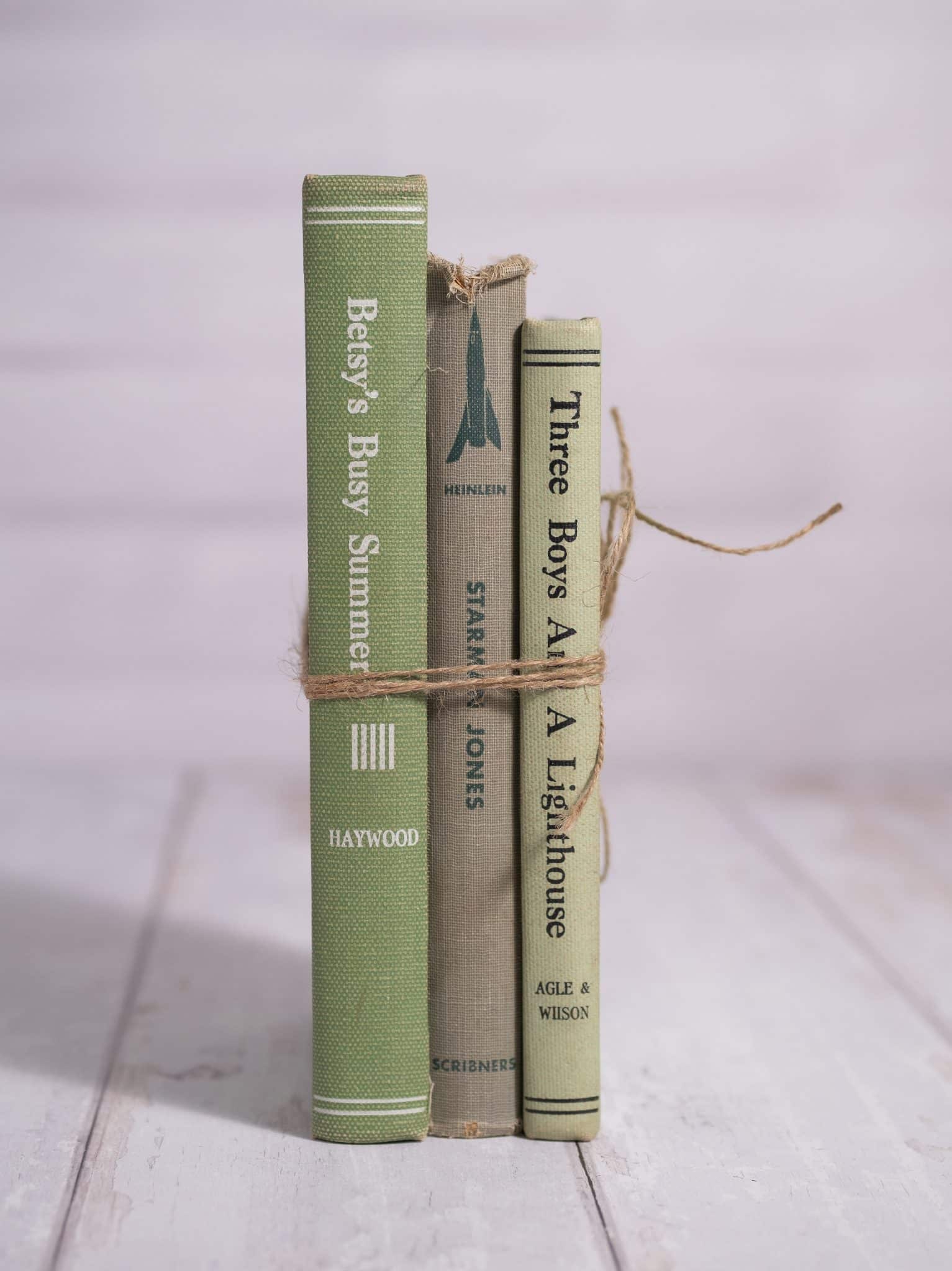 Three green vintage hardcover books tied with natural twine, standing upright on a white wooden floor