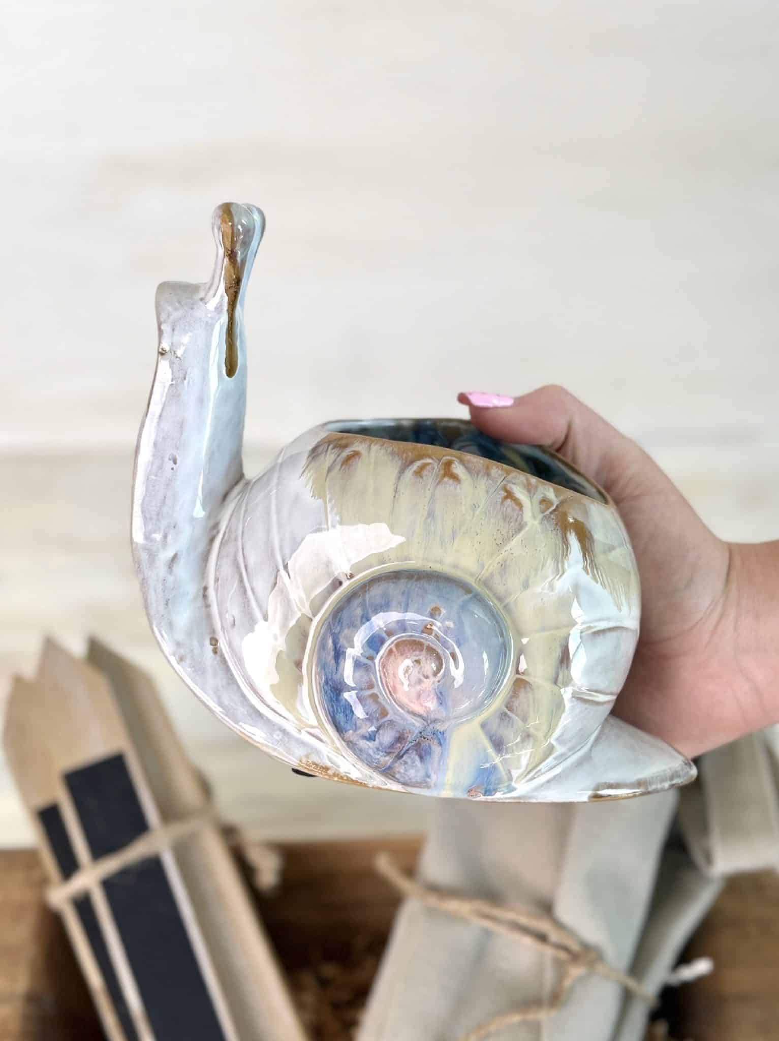 Hand holding a ceramic snail-shaped planter with a glossy, rustic finish.