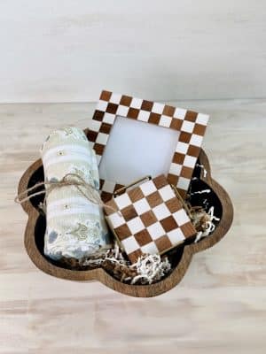 Mother’s Day gift basket with floral towel, checkered frame, and coasters inside a black flower-shaped bowl.