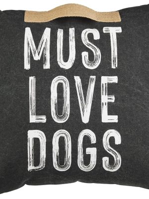 Close-up of the black cotton pillow with bold white “MUST LOVE DOGS” text and a jute handle at the top.