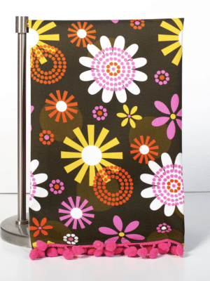Close-up of vintage-style floral tea towel featuring pink chenille pom pom trim and colorful daisy-inspired design.