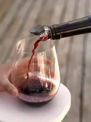 Wine being poured through a mini aerator spout into a stemless glass outdoors.