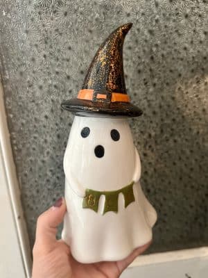 Ceramic ghost figurine with glowing light, black witch hat, and green glitter “BOO” banner.
