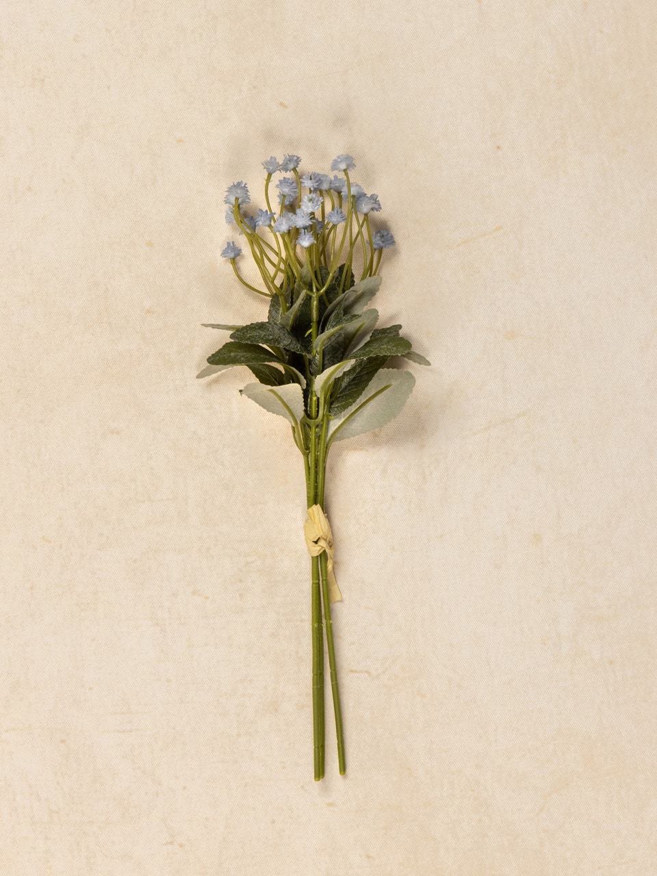 Realistic faux blue flower bundle with green leaves styled in white pedestal vase.
