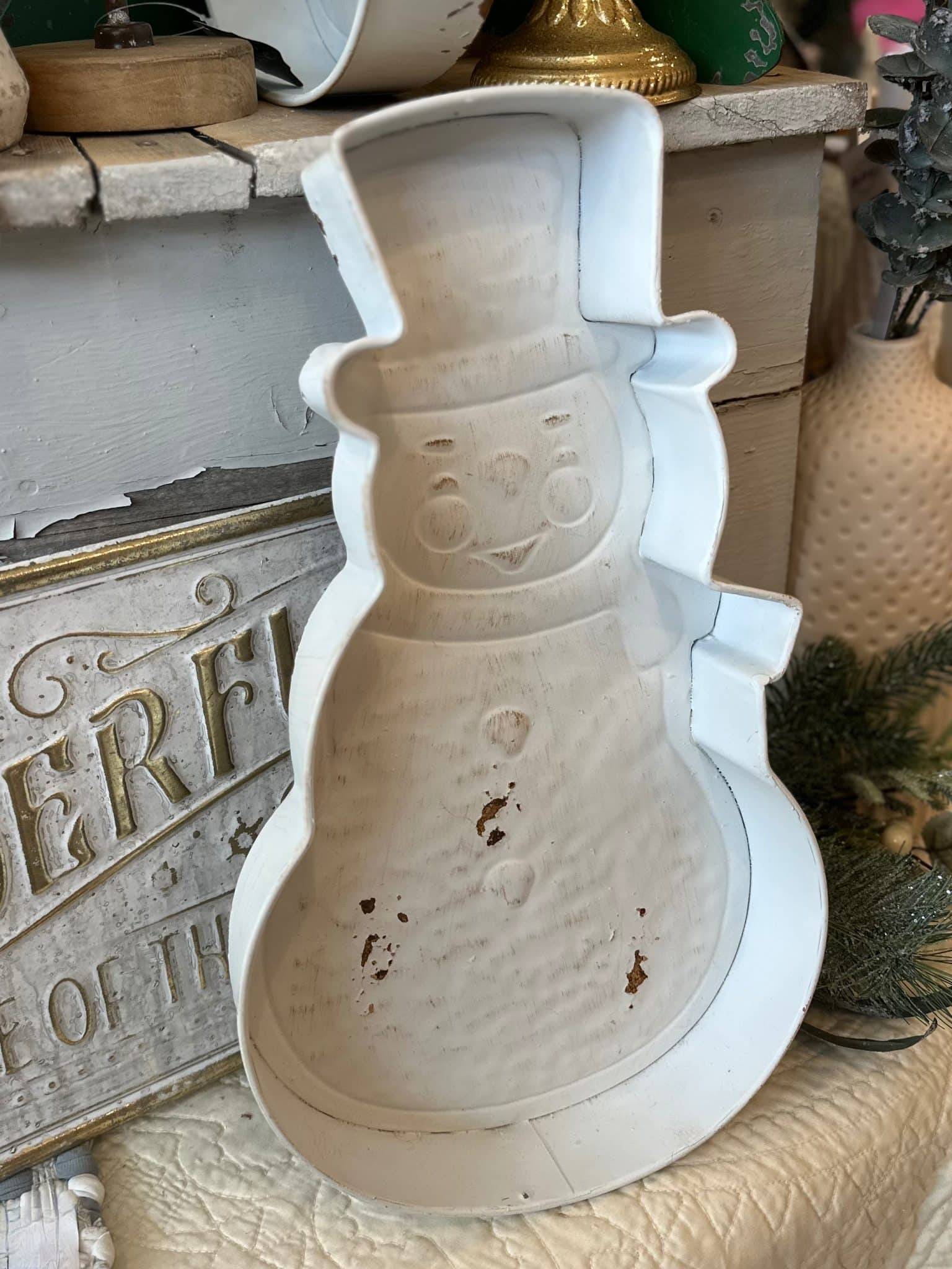 Large distressed white metal snowman tray with carved details displayed in a rustic holiday setup.