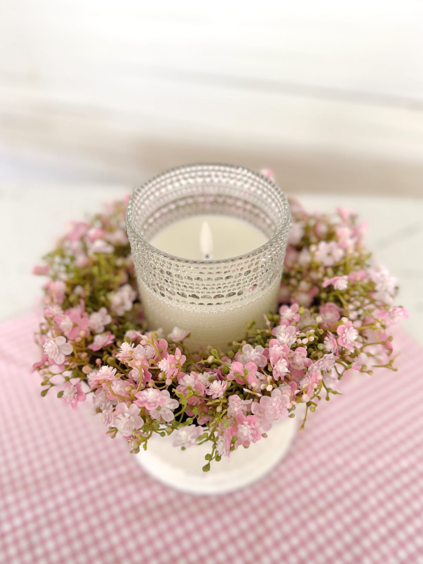 Close-up of a clear dotted glass flameless candle inside a Pink Stardust Blooms Candle Ring styled in a white pedestal bowl.