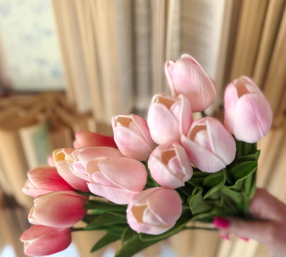 Bright Pink and Light Pink Tulip Bundles held in hand, featuring lifelike pink blooms with fresh green leaves against a vintage book backdrop.