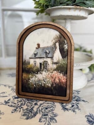 Spring Cottage arched wall art featuring a painted countryside cottage with blooming florals in a warm wood frame.