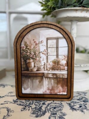 Arched wood framed canvas wall art featuring a rustic farmhouse kitchen sink with florals and sunlit window.
