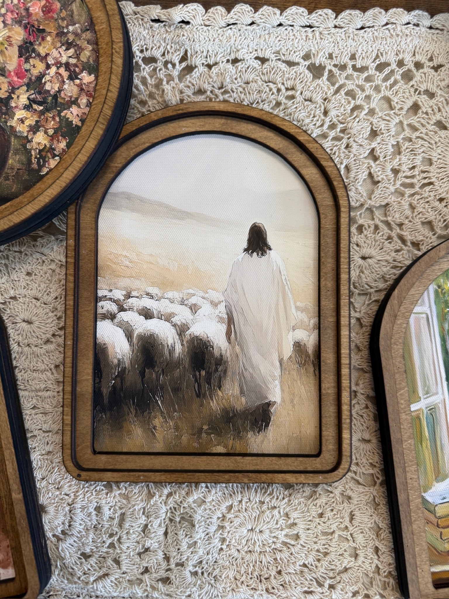 Faith-inspired arched wall decor featuring Jesus walking through a field with sheep in warm neutral hues.