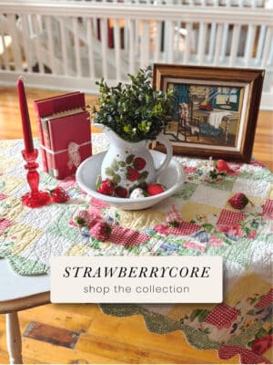 Strawberrycore home decor collection with vintage strawberry pitcher and bowl set, patchwork quilt, glass taper candle holders, and cottagecore accents